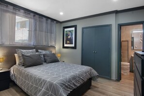 A bedroom with a bed, a nightstand, a framed picture on the wall, a wardrobe, and a door leading to another room.