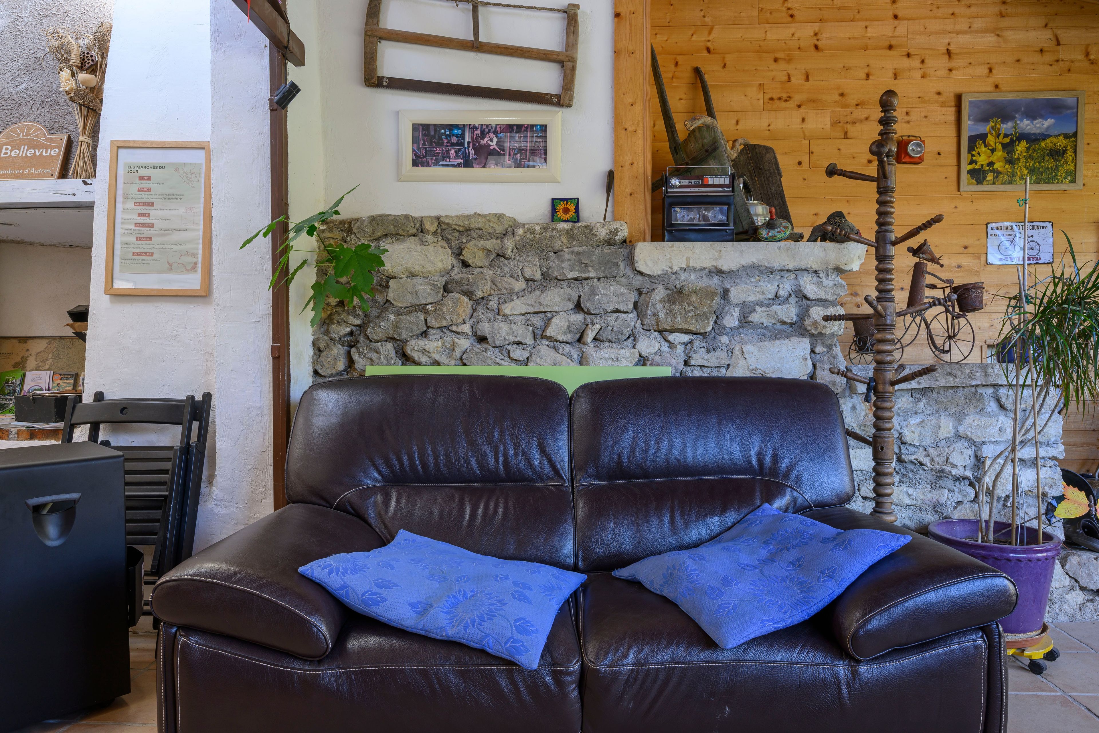 A leather sofa with a blue cushion, a stone wall, a wooden shelf with various items, and a bicycle.