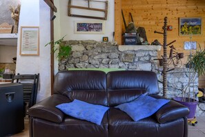 Ein Ledersofa mit blauem Kissen, eine Steinwand, ein Holzregal mit diversen Gegenständen und ein Fahrrad.