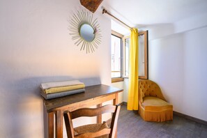 Ein Zimmer mit einem Holztisch, einem Stuhl, einem gelben Vorhang und einem Spiegel an der Wand.