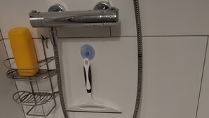 Un espace douche équipé d’un pommeau de douche à main, d’une bouteille jaune et d’une étagère en métal.