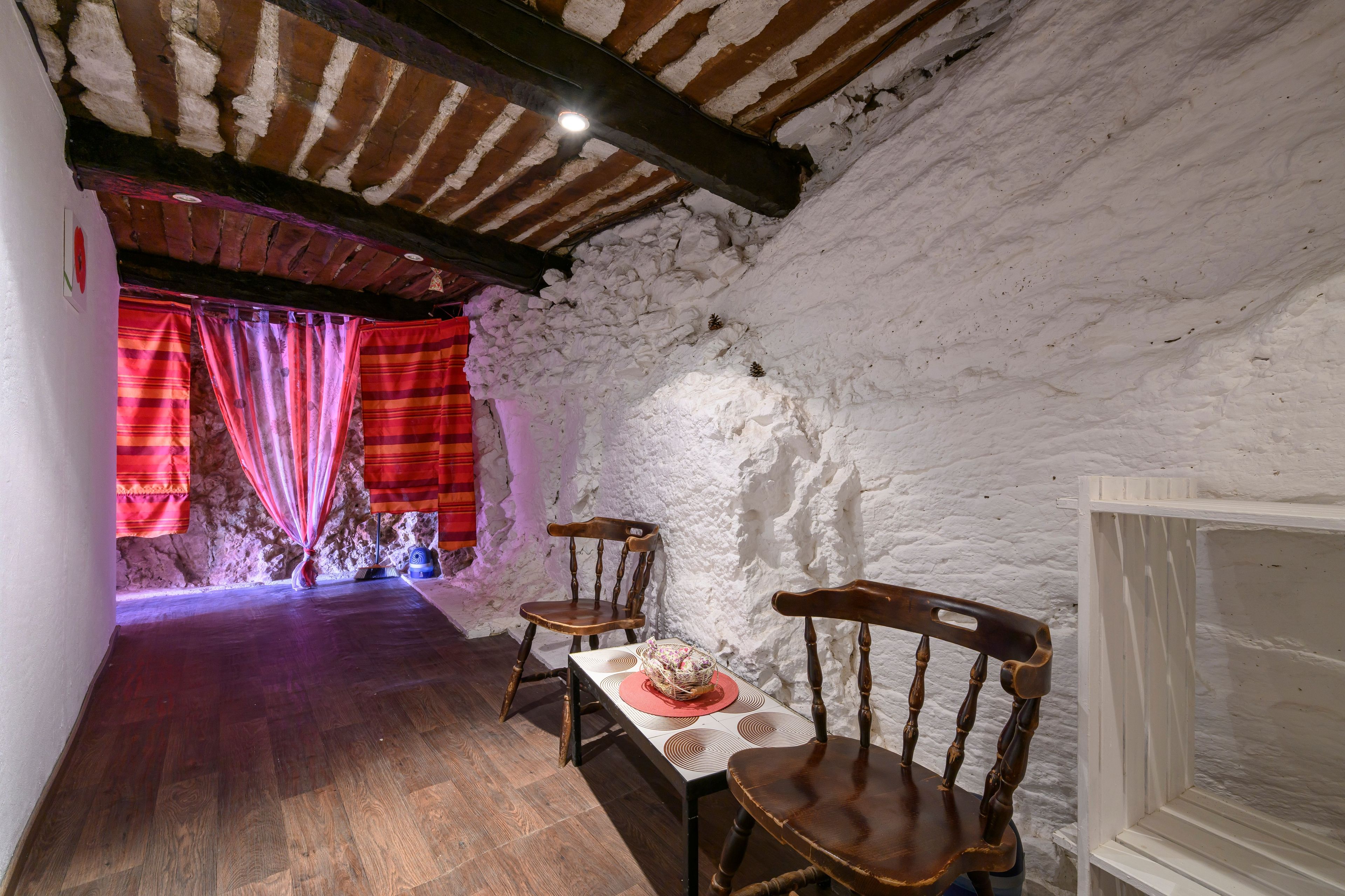 Un intérieur rustique avec des poutres en bois, un mur en pierre et une table entourée de chaises.