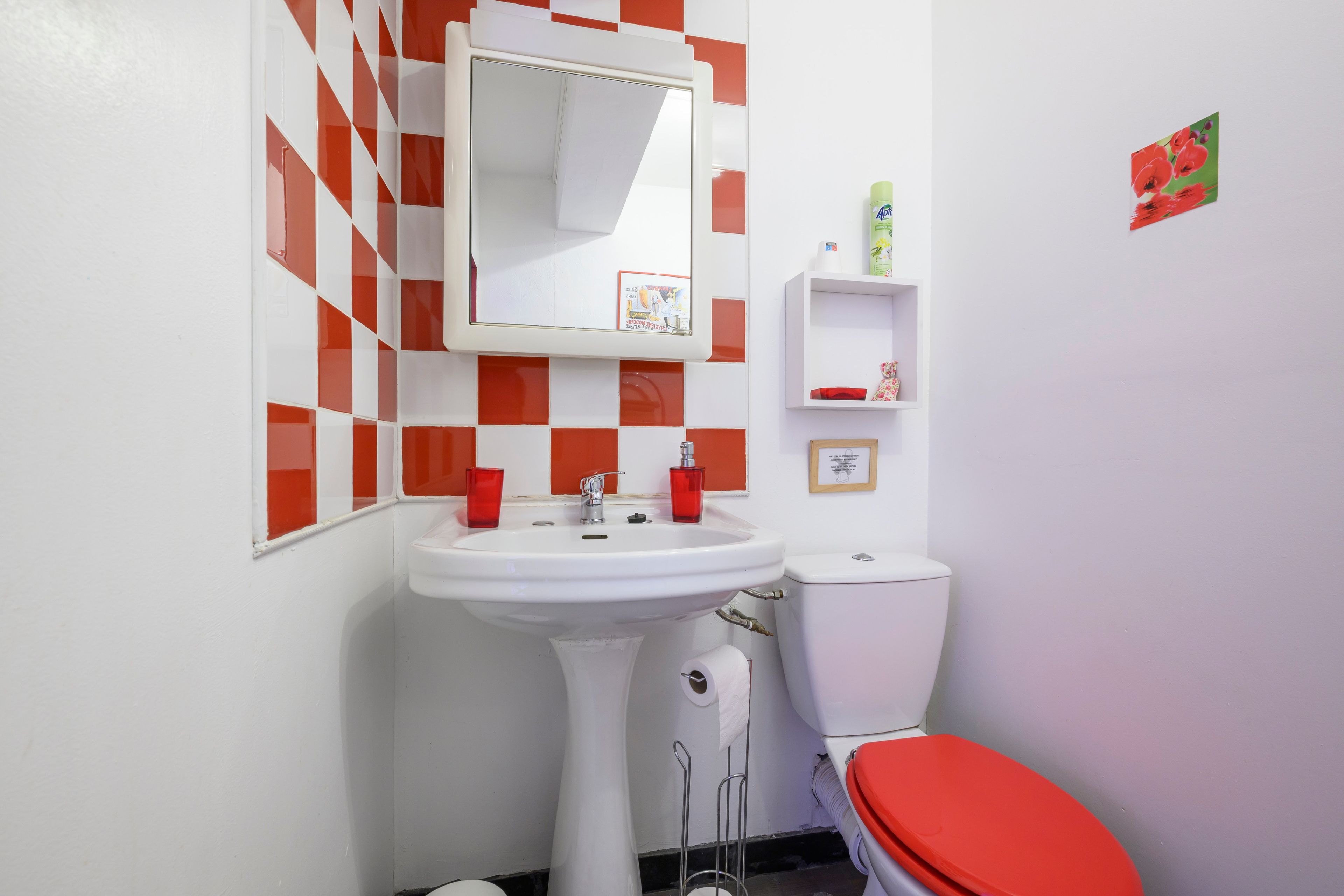 Une salle de bain avec un lavabo blanc, des toilettes rouges et un miroir au-dessus du lavabo.