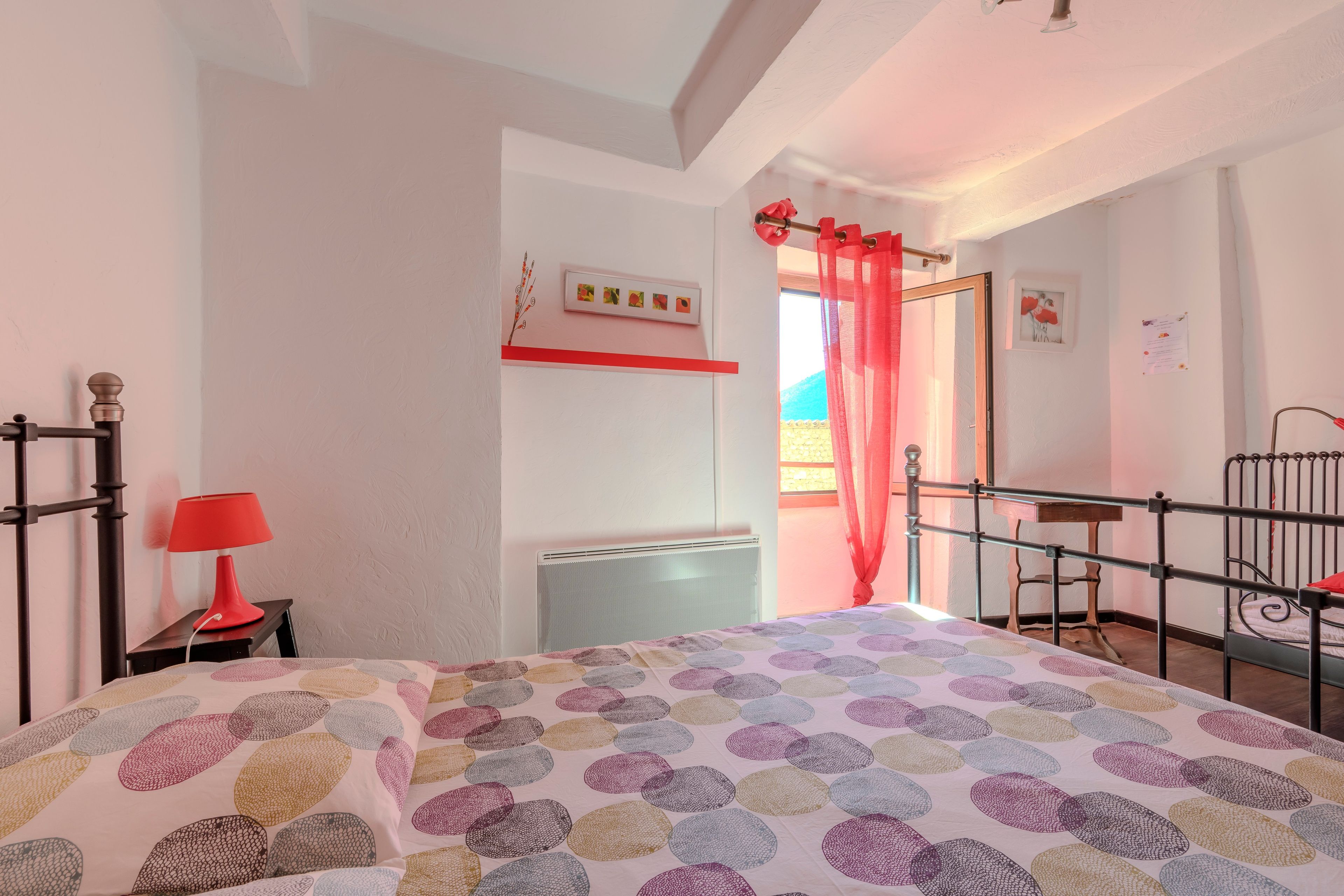 Een slaapkamer met een bed, een rode lamp, een radiator en een raam met een rood gordijn.