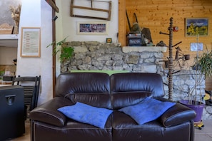 A leather sofa with a blue cushion, a stone wall, a wooden shelf with various items, and a bicycle.