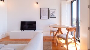 Una sala moderna con televisor de pantalla plana, una mesa de comedor con sillas, un sofá y dos cuadros en la pared.