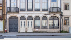 Un edificio con fachada simétrica, que presenta un ventanal central arqueado con vidrio decorativo, flanqueado por dos juegos de puertas y ventanas a cada lado.