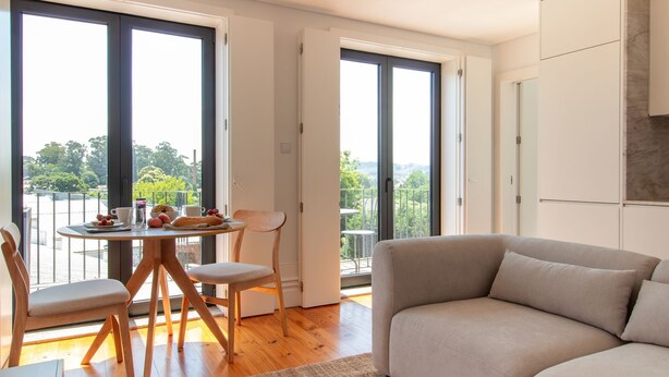 Una sala de estar moderna con sofá, una mesa de comedor con sillas y un balcón con vistas a zonas verdes.