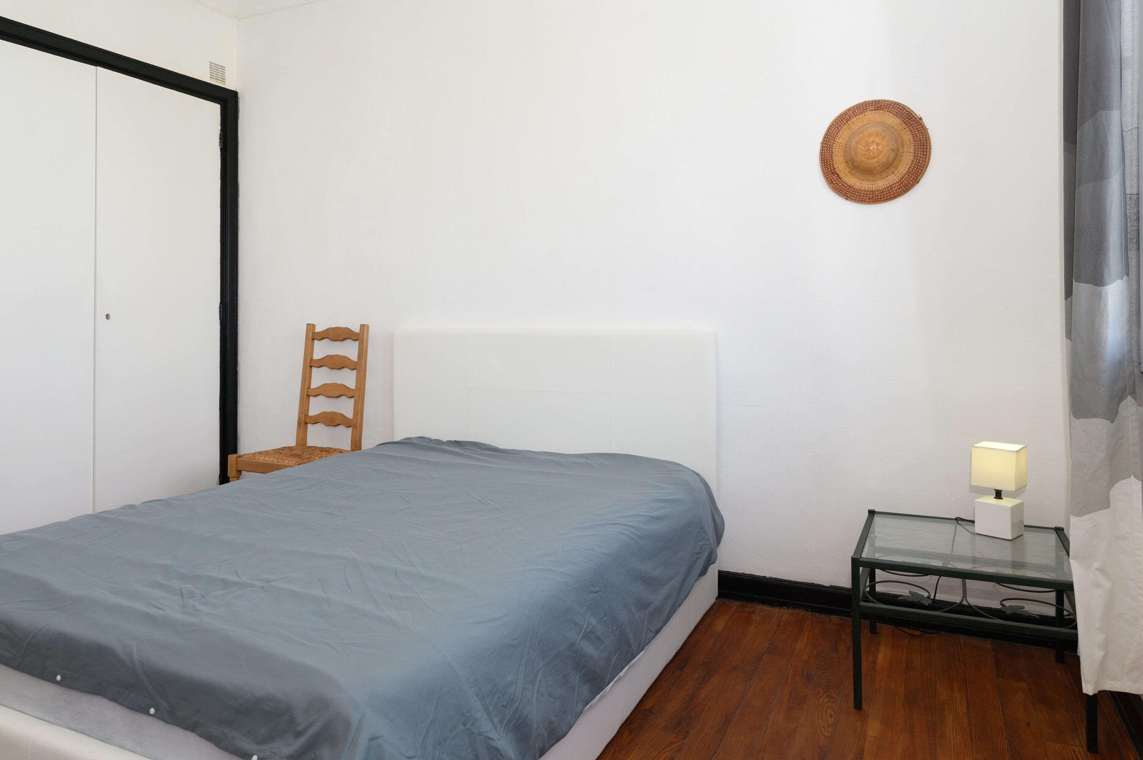 A bedroom with a bed, a chair, a bedside table with a lamp, and a wall-mounted hat.