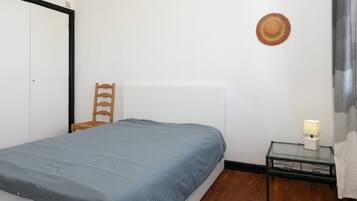 A bedroom with a bed, a chair, a bedside table with a lamp, and a wall-mounted hat.