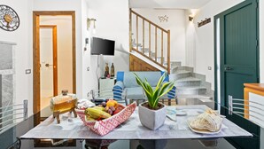 Un comedor con una mesa dispuesta para dos personas, una planta en maceta y una cesta de fruta.