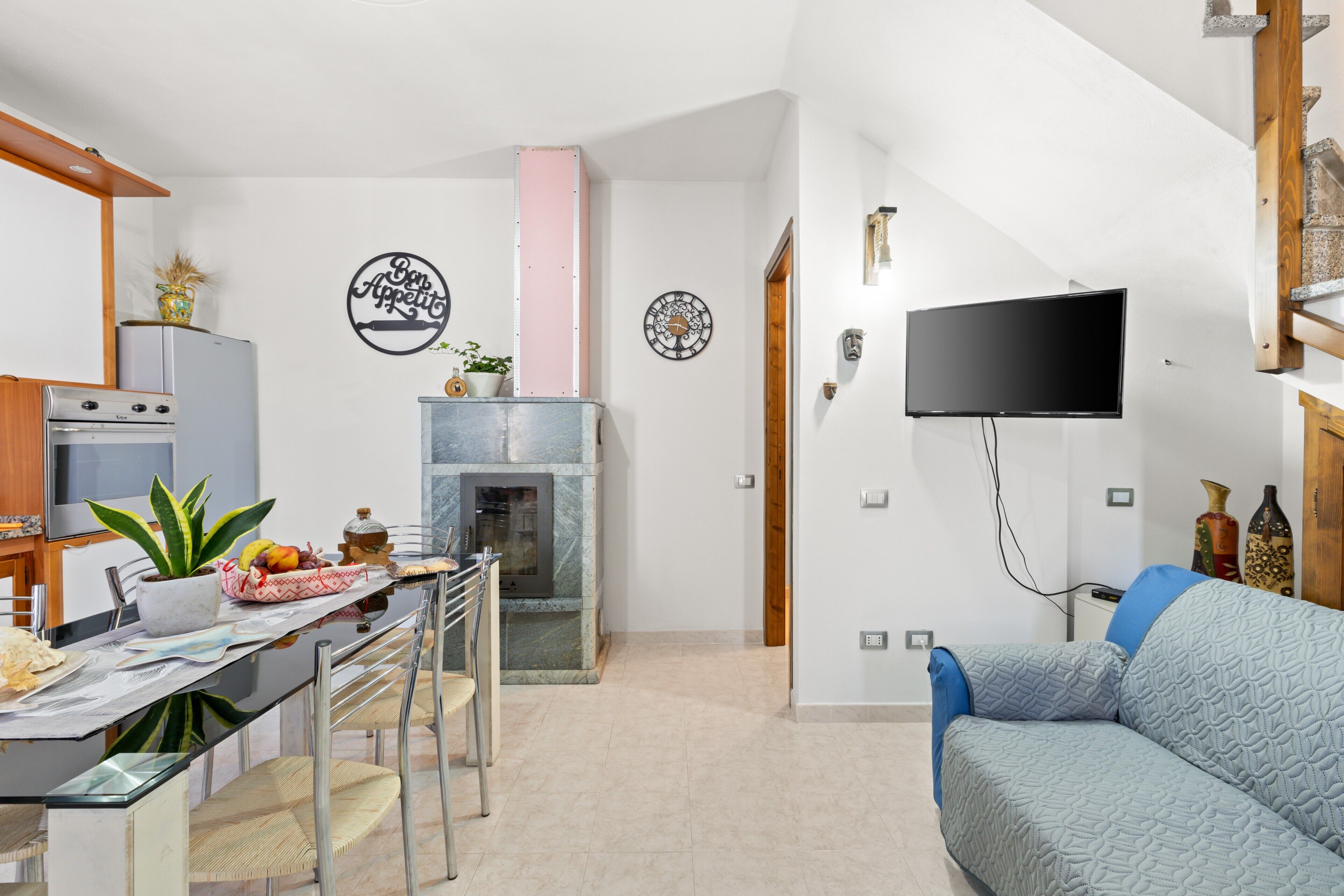 A modern kitchen with a dining area, a flat-screen TV, and a blue sofa.