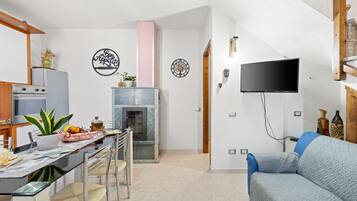 A modern kitchen with a dining area, a flat-screen TV, and a blue sofa.