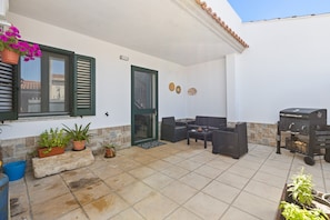 A patio with outdoor furniture, a grill, and potted plants.