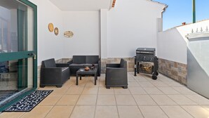 Un patio con mobiliario de mimbre, una parrilla y suelo de baldosas.