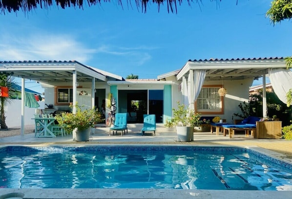 A swimming pool with lounge chairs and potted plants, surrounded by a covered patio area.