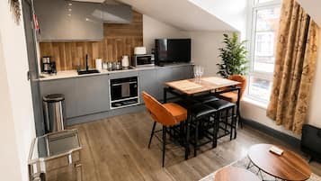 A modern kitchen with grey cabinets, a microwave, and a TV. There is a dining area with a wooden table and orange chairs.
