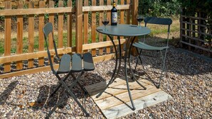 Une terrasse avec une table ronde et deux chaises, une bouteille de vin et un verre de vin rouge posés sur une plateforme en bois.
