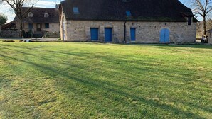 A stone building with a sloped roof and blue shutters, surrounded by a grassy field. - Quercy farmhouse (cajarc)
