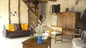 A rustic living room with exposed wooden beams, a sofa with yellow cushions, a wooden table with a vase of dried flowers, and a wooden chair. - Quercy farmhouse (cajarc)
