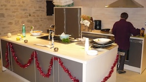 A kitchen with a central island, a sink, a stove, and a range hood. There is a person cooking at the stove. - Quercy farmhouse (cajarc)