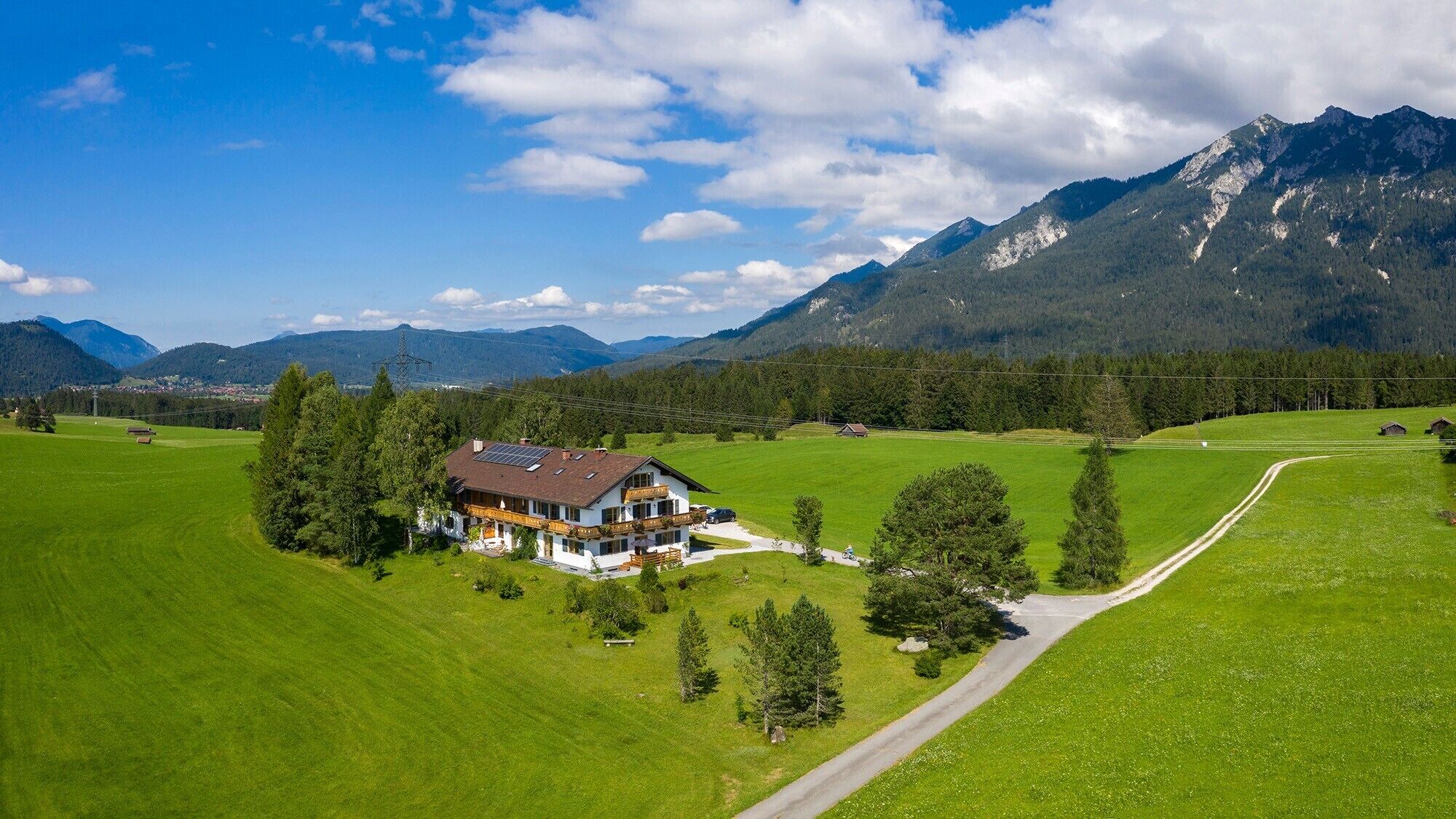 Ein großes Haus mit Schrägdach, umgeben von grünen Feldern und Bergen.