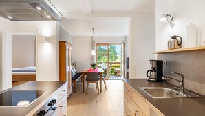 A modern kitchen with a built-in stove, a sink, and a dining area with a table and chairs. - Apartment '180 Grad' with Mountain View, Private Terrace and Wi-Fi (Mittenwald)