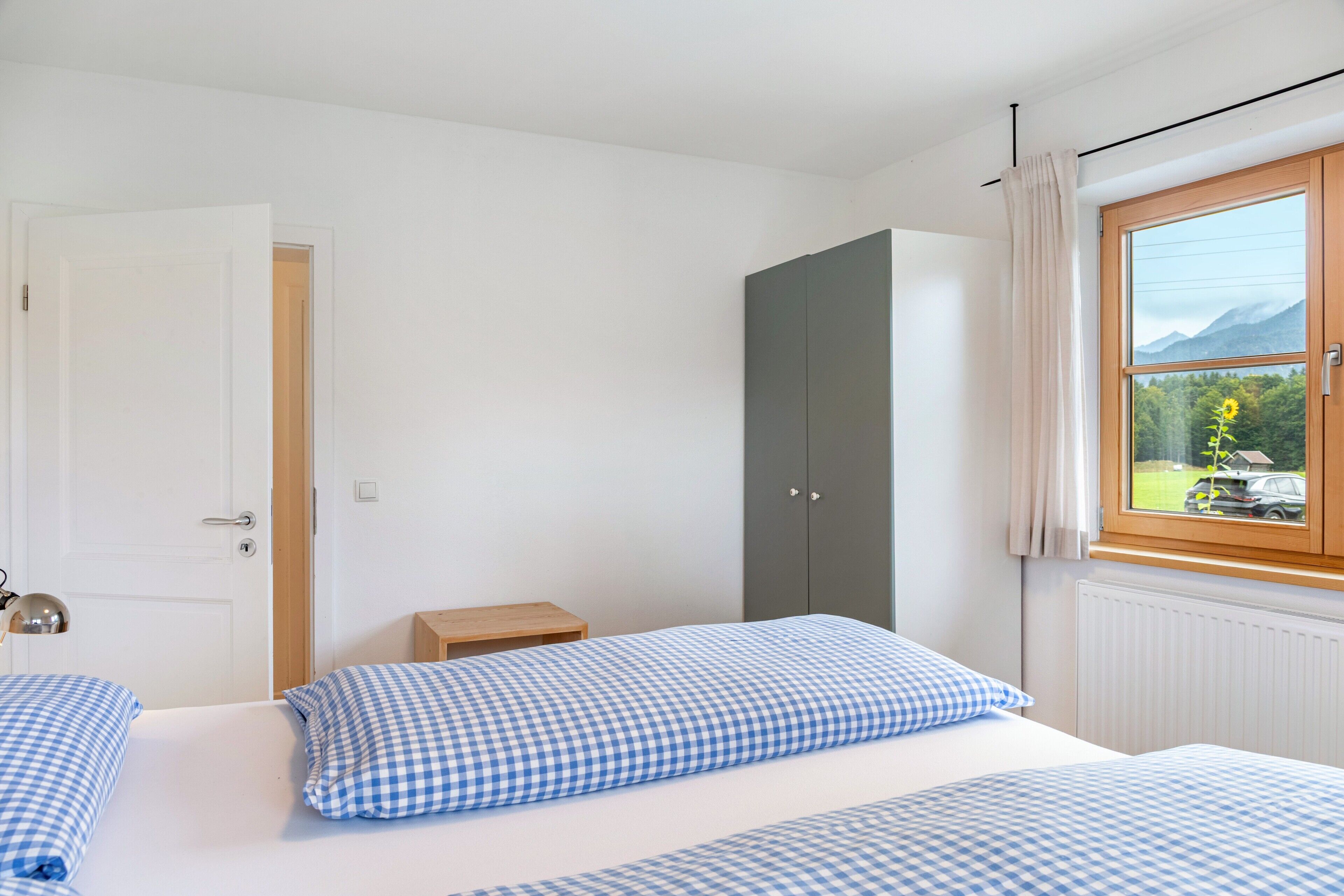 A bedroom with two beds, a wardrobe, a window with a view, and a door.