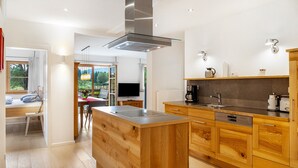 A modern kitchen with wooden cabinets, a central island, and a built-in stove. - Apartment '180 Grad' with Mountain View, Private Terrace and Wi-Fi (Mittenwald)