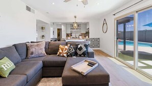 Ein modernes Wohnzimmer mit einem Ecksofa, einem Couchtisch und Blick auf einen Swimmingpool durch große Schiebeglasüren.