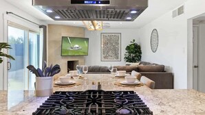 Eine moderne Küche mit Kochinsel, Edelstahl-Dunstabzugshaube und Essbereich mit Sofa und Esstisch.