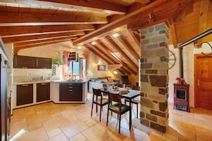 A rustic kitchen with wooden beams, a stone wall, and a fireplace.