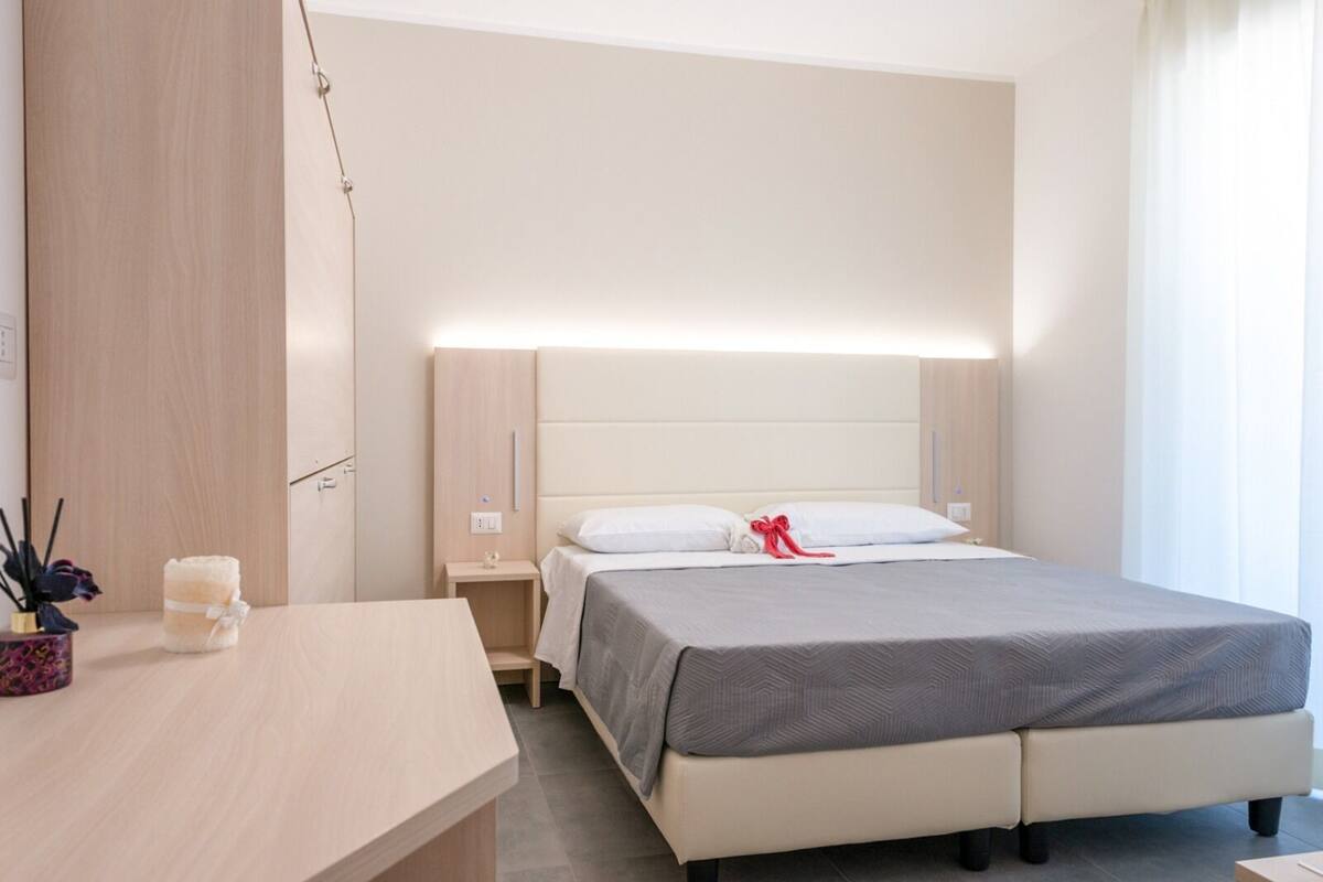 A modern hotel room with a large bed, bedside tables, a desk, and a nightstand.