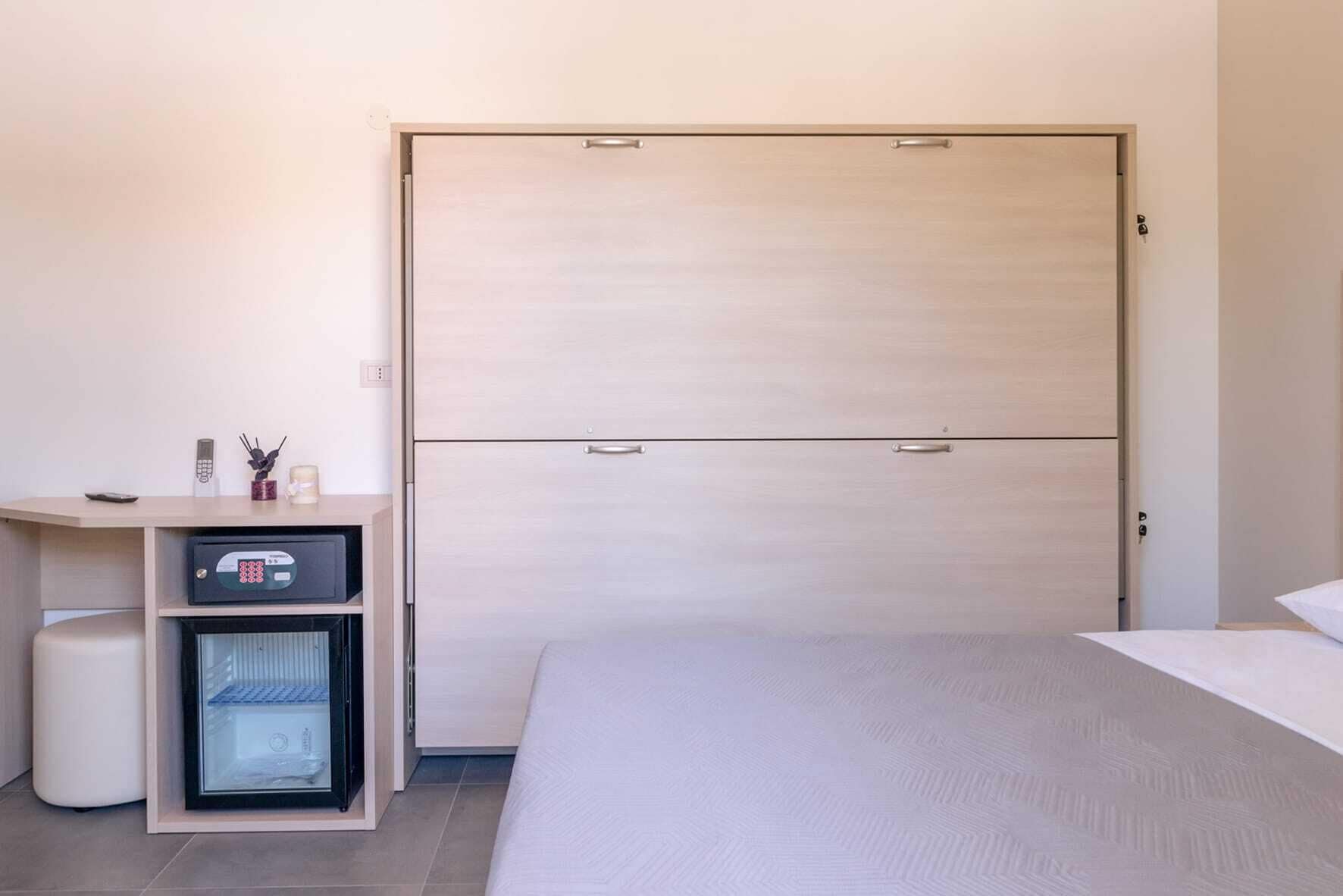 Une chambre d’hôtel comprenant un lit, une table de chevet avec un petit réfrigérateur et une armoire.