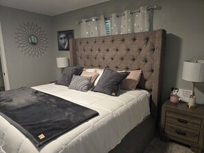 A bedroom with a tufted headboard, a bed with multiple pillows, a bedside table with a lamp, and a wall decoration.