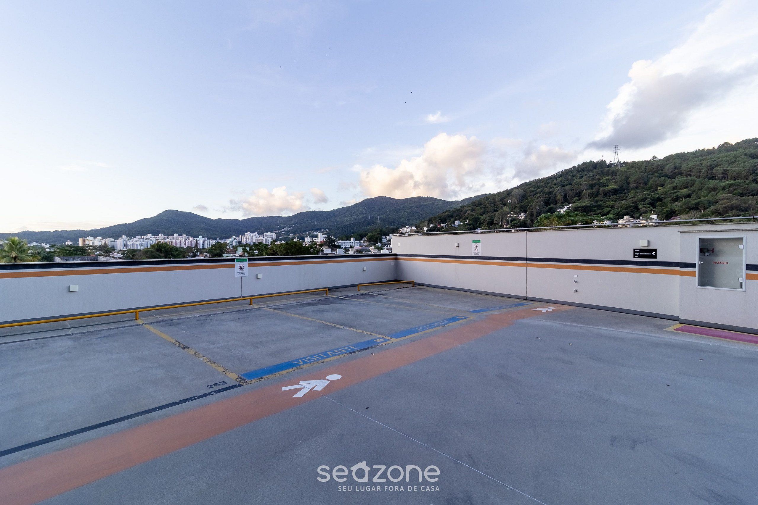 Un estacionamiento en la azotea con vistas a un paisaje urbano y montañas al fondo.