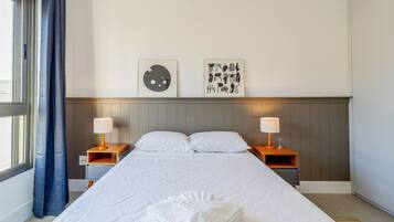 A hotel room with a large bed, two bedside tables with lamps, a headboard, and two wall art pieces.