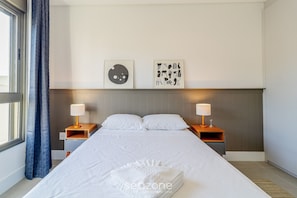 A hotel room with a large bed, two bedside tables with lamps, a headboard, and two wall art pieces. - Stay in a Building With a Pool, Gym, and Leisure - SSL (Florianópolis)