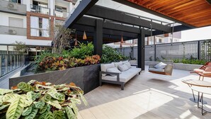A modern outdoor patio with a wooden ceiling, a built-in seating area, and a variety of plants. - Stay in a Building With a Pool, Gym, and Leisure - SSL (Florianópolis)
