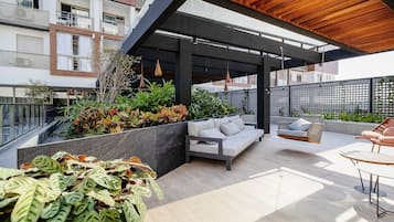Un patio moderno al aire libre con techo de madera, zona de estar integrada y diversas plantas.