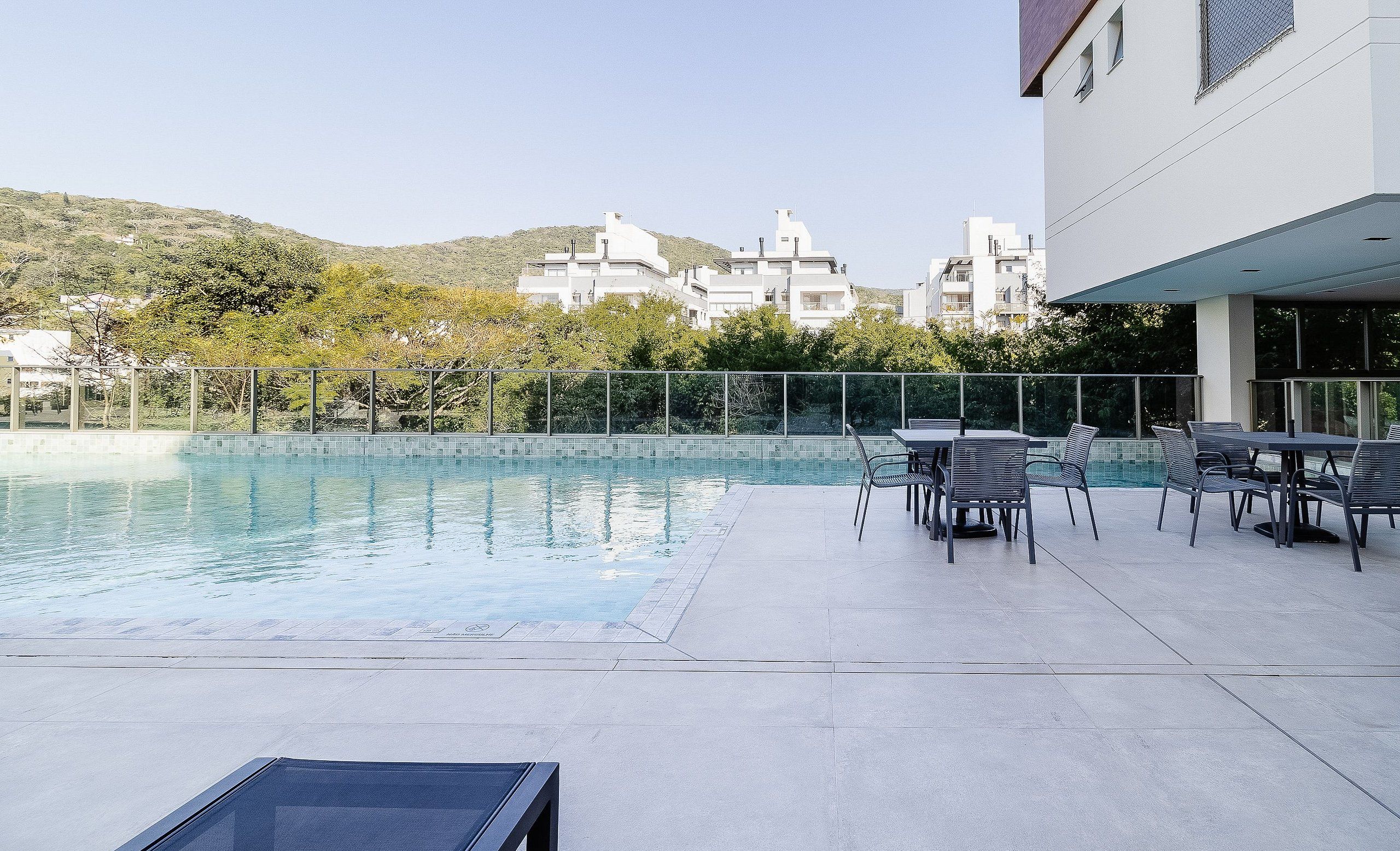 A swimming pool with a patio area, surrounded by a metal fence and trees.