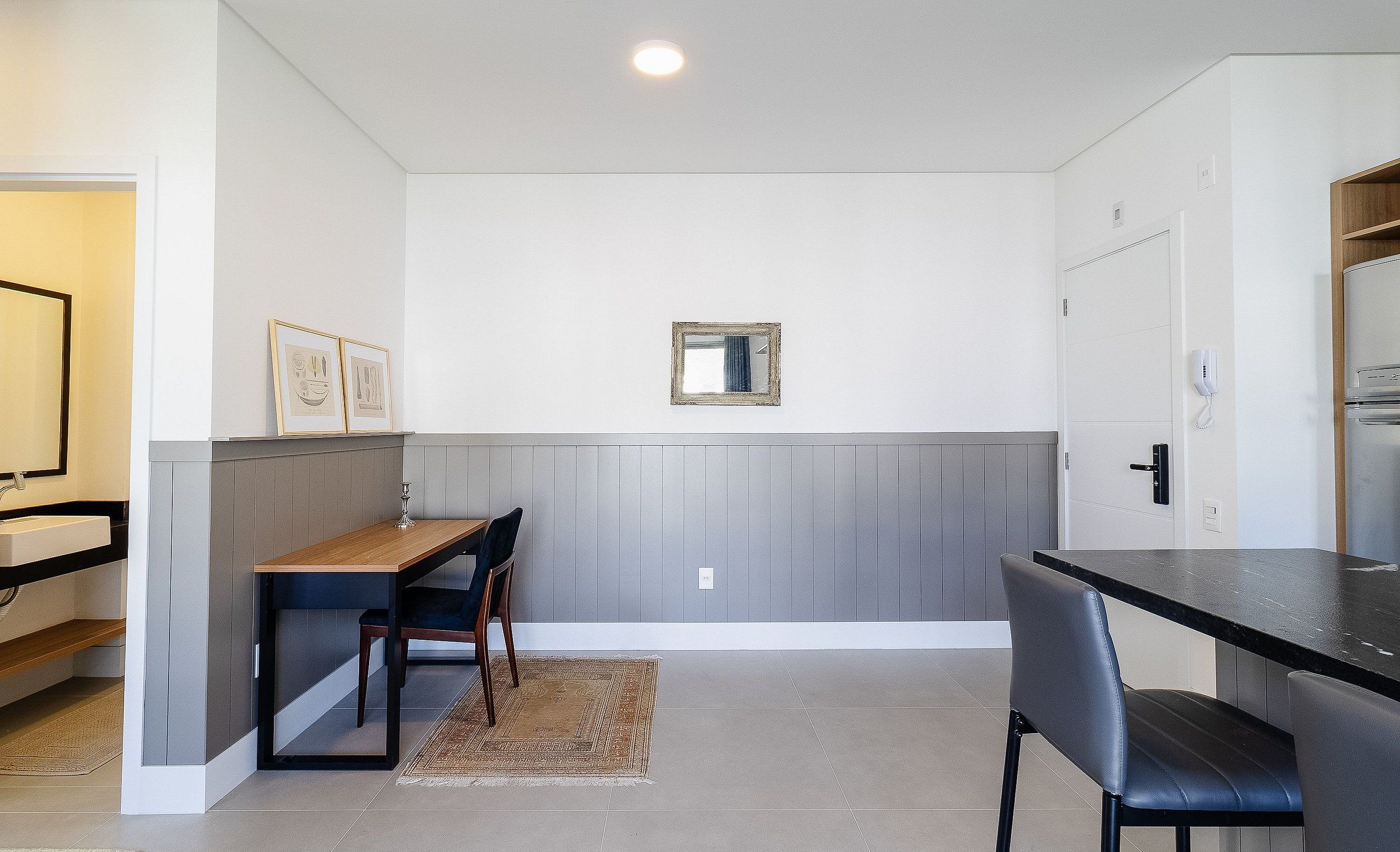 A modern kitchen with a wooden table and chairs, a small mirror on the wall, and a refrigerator.