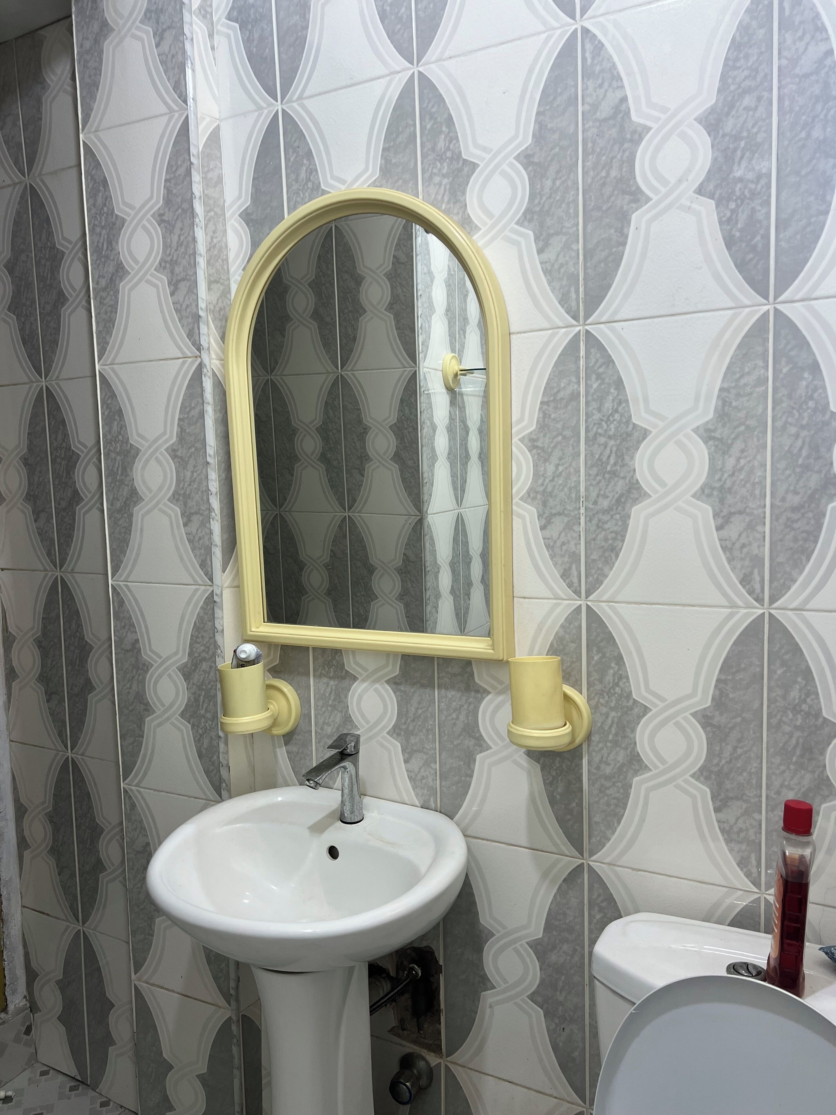 Een badkamer met een wit wastafel, een spiegel met een gele lijst, en een toilet.