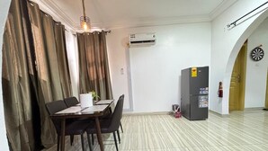 Un comedor con una mesa, sillas, un lámpara colgante, un equipo de aire acondicionado, un refrigerador y un dardo en la pared.