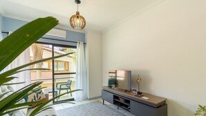 A modern living room with a large window, a flat-screen TV, a wooden console table, and a hanging light fixture. - Apt With Barbecue in Lagoa da Conceicao Sro0002 (Florianópolis)