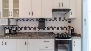 A modern kitchen with white cabinets, a microwave, a coffee maker, a water dispenser, and a stove. - Apt With Barbecue in Lagoa da Conceicao Sro0002 (Florianópolis)