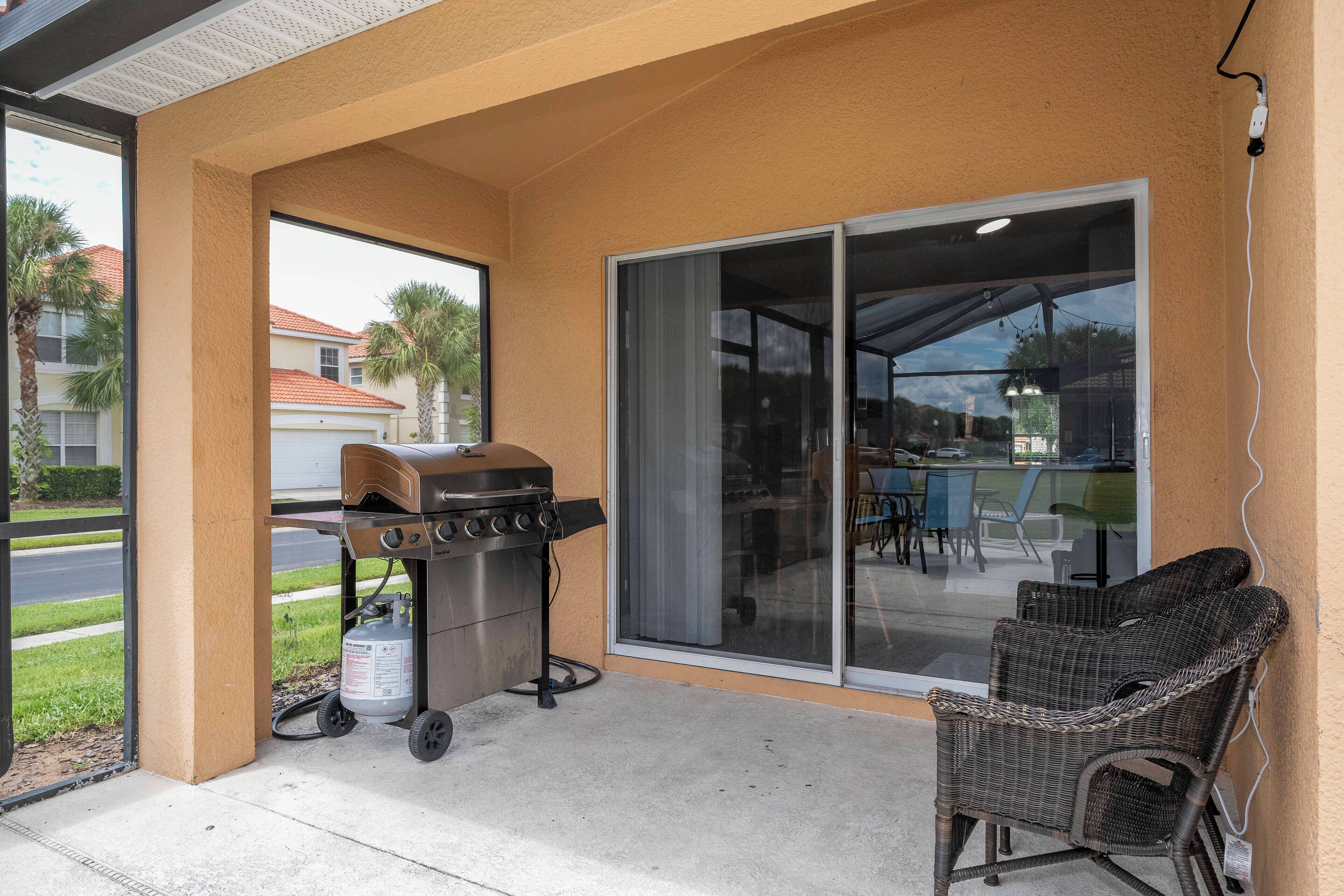 Un patio techado con una parrilla, una silla de mimbre y un ventanal corredizo que da a otra área de patio.