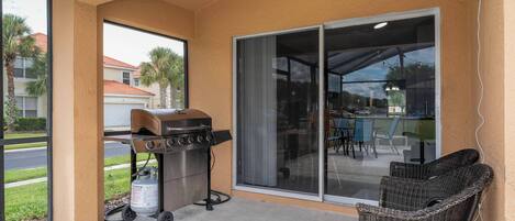 Un patio techado con una parrilla, una silla de mimbre y un ventanal corredizo que da a otra área de patio.