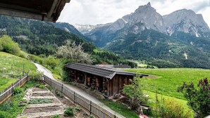 Un edificio rústico de madera con techo inclinado, rodeado por un valle verde exuberante y montañas al fondo.