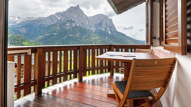 Un balcón de madera con una mesa y una silla, con vistas a un paisaje montañoso.